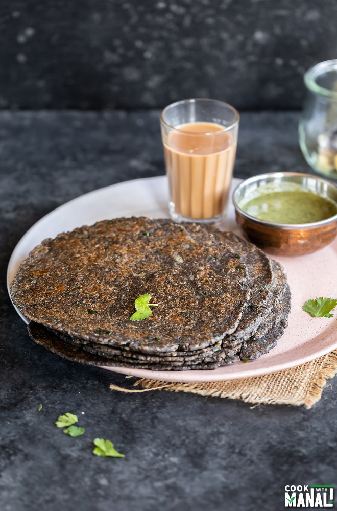 stack of kuttu paratha on a plate with glass of chai in the background with bowl of chutney on the side