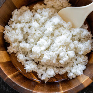 white rice in a wooden bowl with a rice paddle