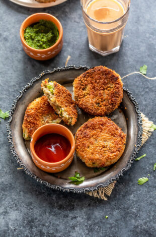 3 veg cutlet placed on a plate with a bowl of ketchup and bowl of chutney and glass of chai in the background