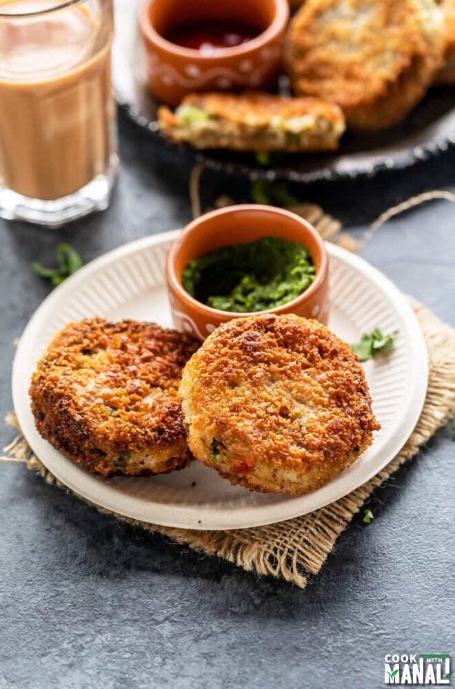 2 veg cutlet in a plate with bowl of cilantro chutney and glass of chai in the background