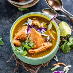 soup bowl topped with samosa, cilantro, sliced cabbage with lime wedge on the side