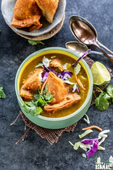 soup bowl topped with samosa, cilantro, sliced cabbage with lime wedge on the side
