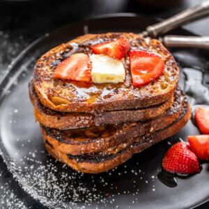 stack of French toast topped with butter and strawberries with bowl of strawberries in the background