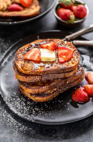 stack of French toast topped with butter and strawberries with bowl of strawberries in the background