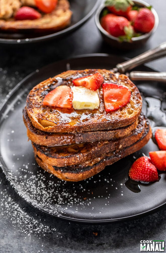 stack of French toast topped with butter and strawberries with bowl of strawberries in the background