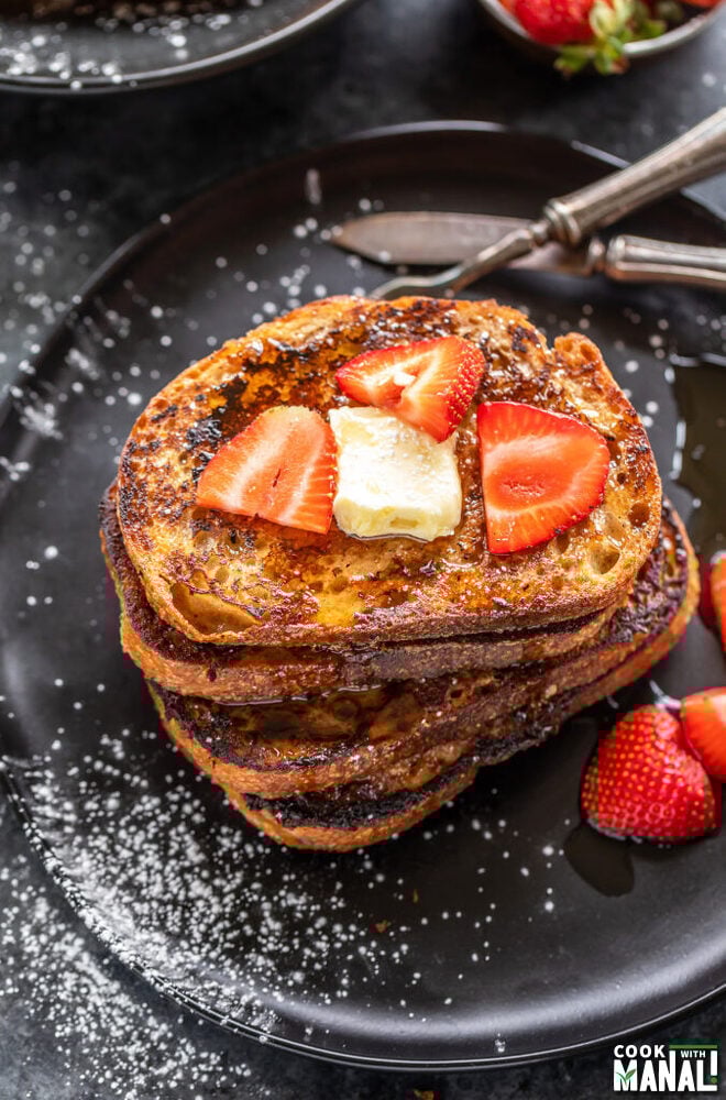 stack of French toast topped with butter and strawberries with bowl of strawberries in the background