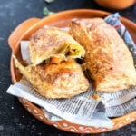 a veg puff cut into half to reveal the filling and a cup of chai placed in the background