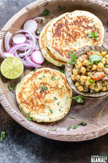 bread kulcha served with a bowl of matar chaat, sliced onion and a round of lemon in a pattal