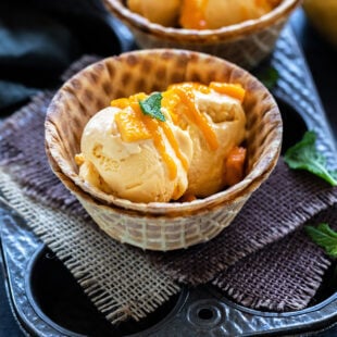 mango ice cream served in a waffle bowl topped with fresh mangoes, mint leaves and drizzled with mango puree