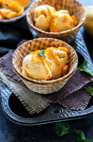 mango ice cream served in a waffle bowl topped with fresh mangoes, mint leaves and drizzled with mango puree