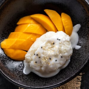 sticky rice topped with coconut sauce and served with sliced mangoes on the side in a black bowl