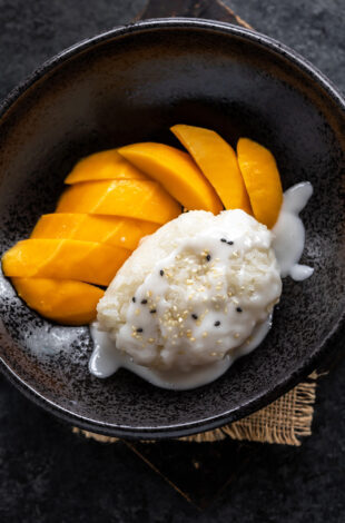 sticky rice topped with coconut sauce and served with sliced mangoes on the side in a black bowl