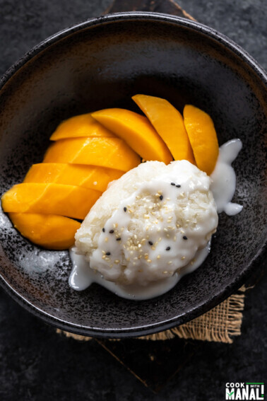 sticky rice topped with coconut sauce and served with sliced mangoes on the side in a black bowl