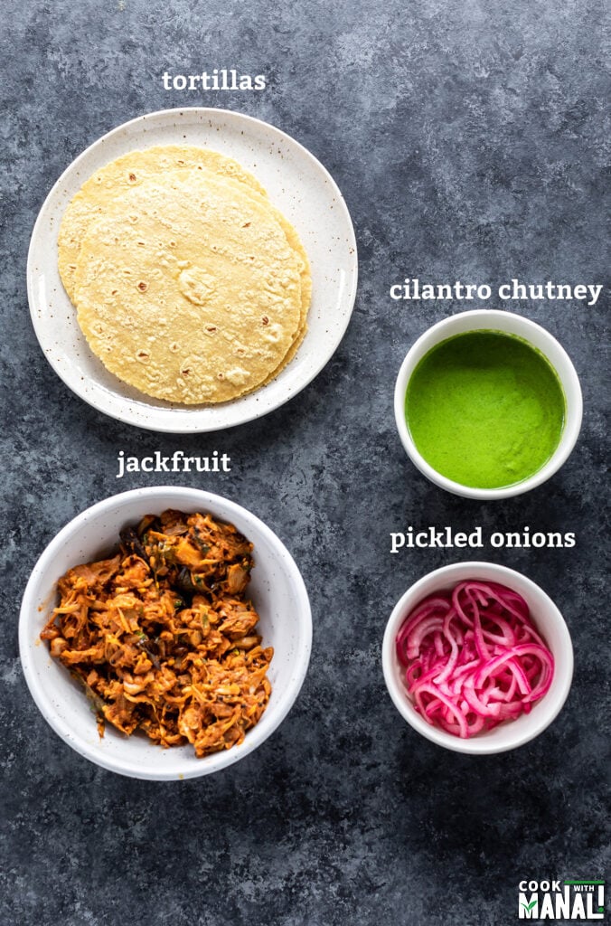 plate with tortillas, 1 bowl filled with jackfruit masala and 2 smaller bowls with chutney and pickled onions