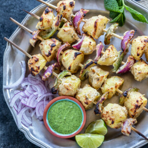 grilled baby potatoes, onions and peppers arranged on skewers with a bowl of chutney on the side