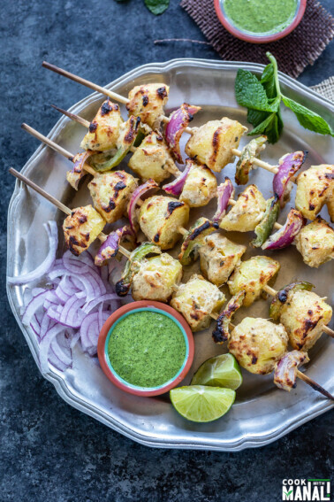 grilled baby potatoes, onions and peppers arranged on skewers with a bowl of chutney on the side