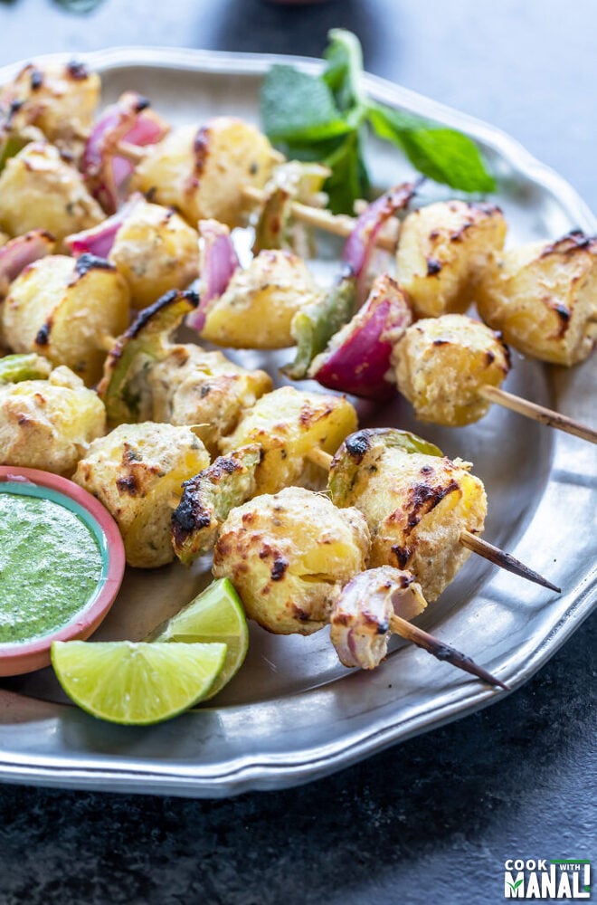 grilled baby potatoes, onions and peppers arranged on skewers with a bowl of chutney and lime wedge on the side