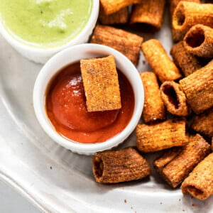 pasta chips served in a plate with 1 bowl of chutney and another bowl of hot sauce