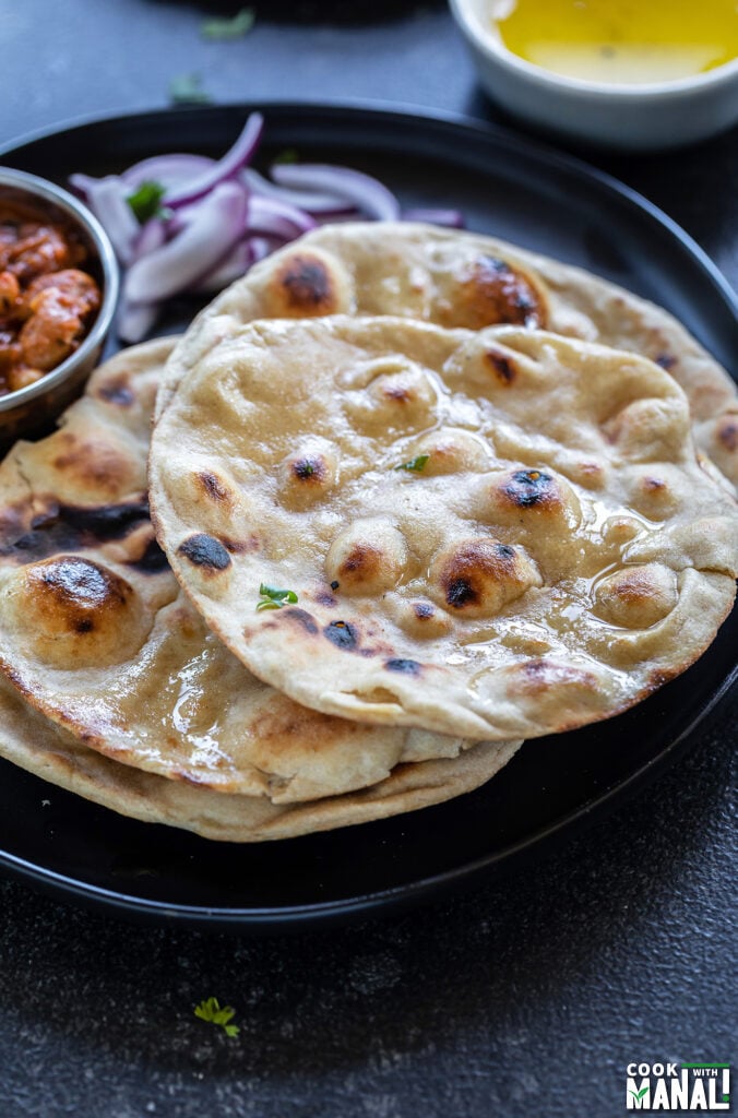 rotis arranged on a plate with a bowl of creamy curry and another bowl of ghee in the background