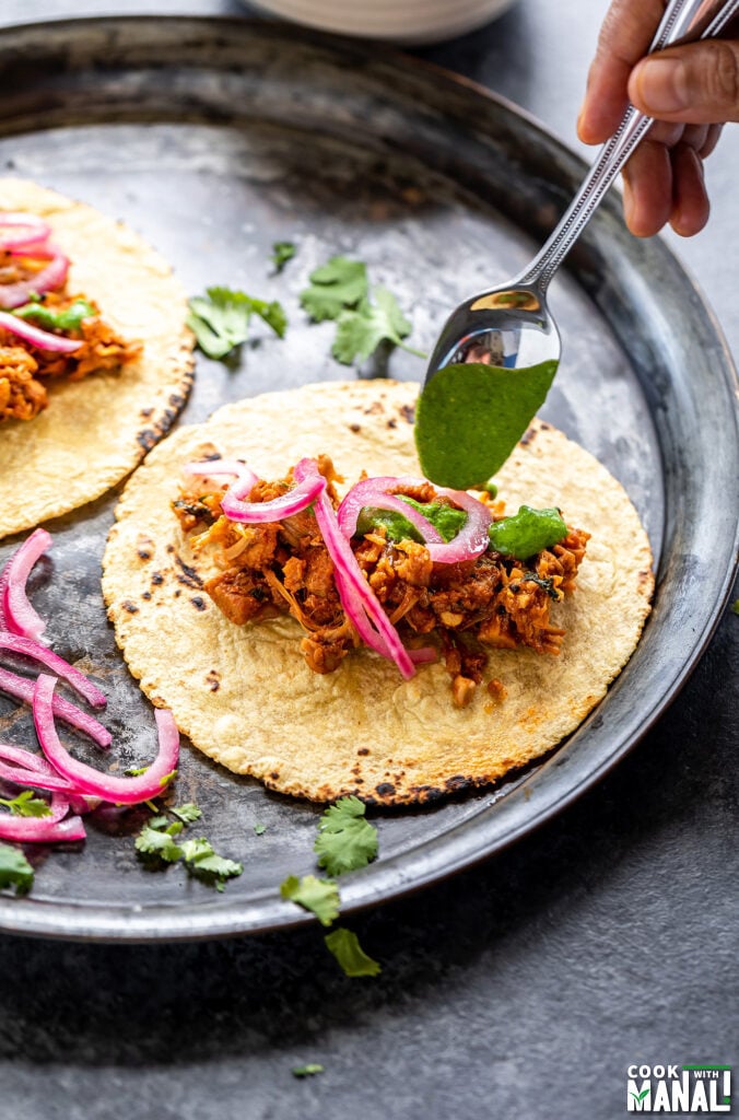 cilantro chutney being drizzled on top of tacos with a spoon