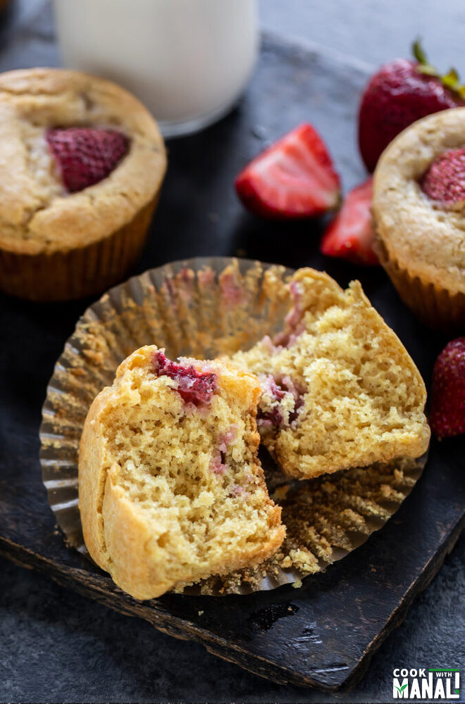 a muffin cut in half to show in interior and few strawberries placed on the side