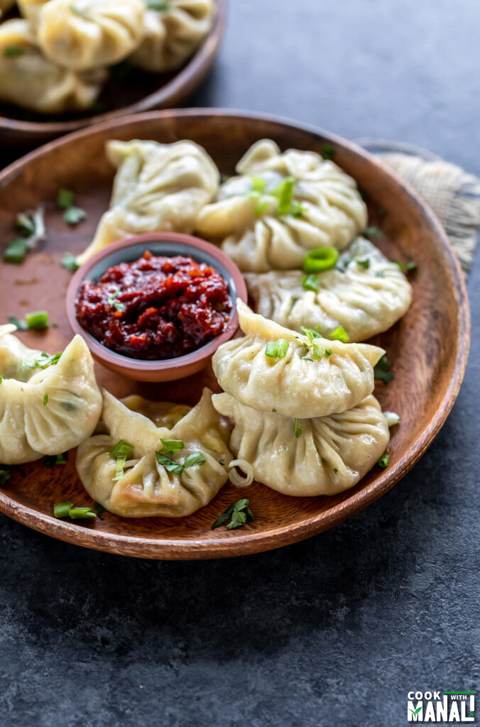 steamed momos placed on a wooden plate with a bowl of hot sauce on the side