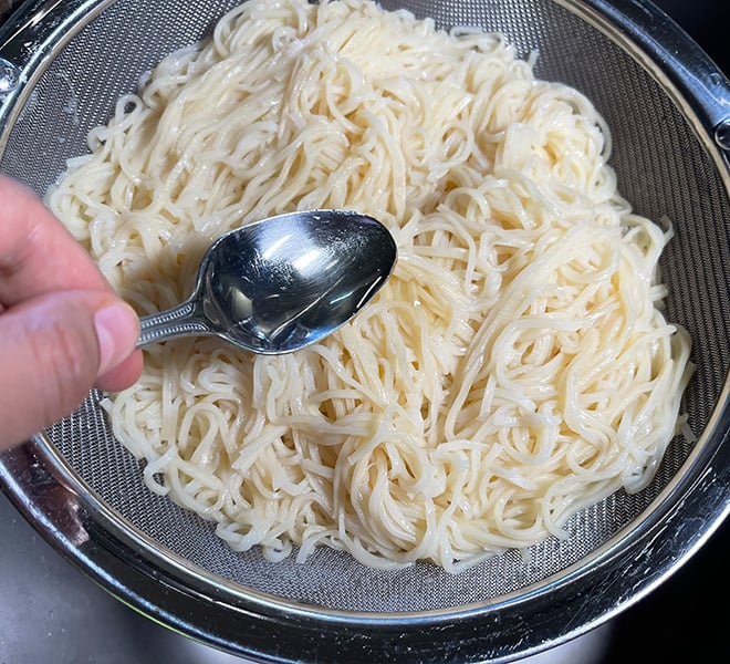 oil being drizzled on boiled noodles