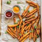 french fries coated with spices placed on a baking tray with 2 bowls of dipping sauces