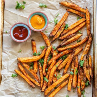 french fries coated with spices placed on a baking tray with 2 bowls of dipping sauces