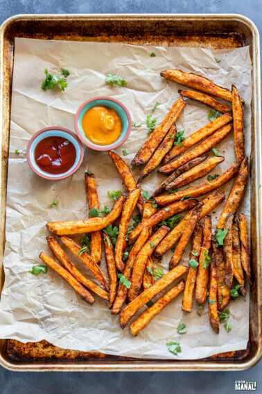 french fries coated with spices placed on a baking tray with 2 bowls of dipping sauces