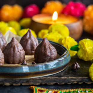 chocolate modaks placed on a plate with garlands placed on sides and candles in the background