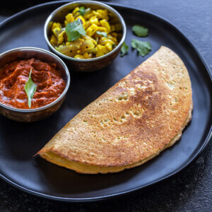 a dosa served on a plate with a bowl of chutney and a bowl of paneer