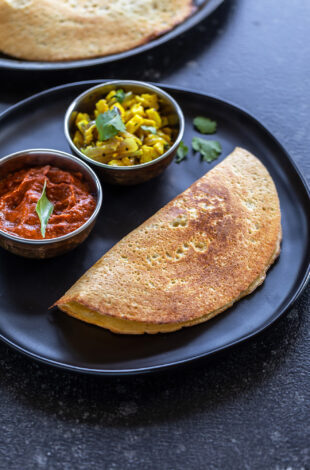 a dosa served on a plate with a bowl of chutney and a bowl of paneer