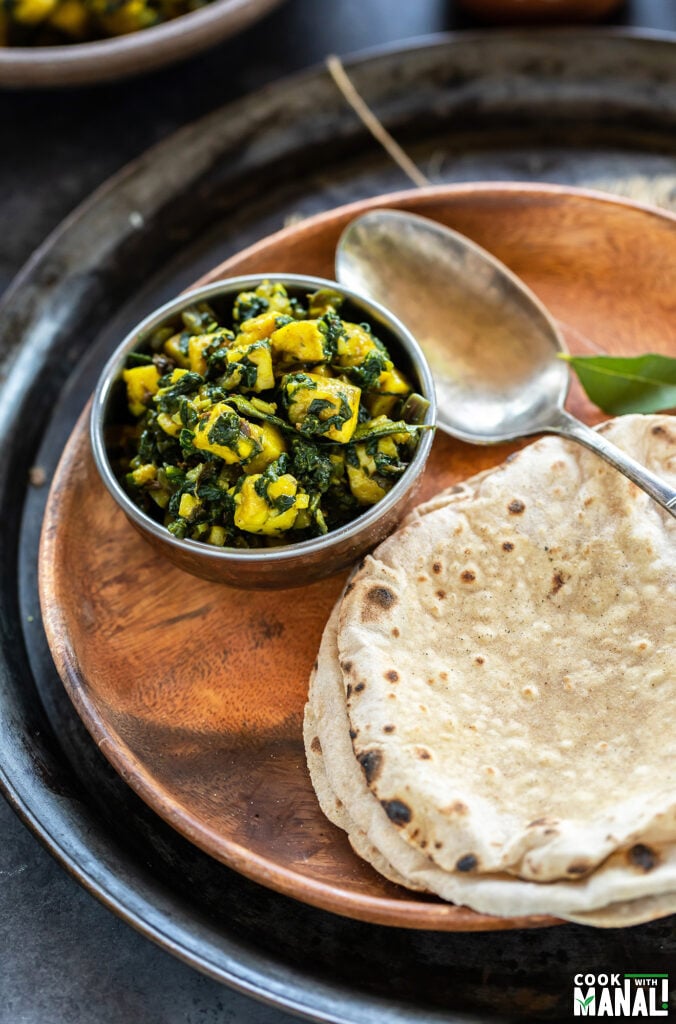 spinach paneer served in a copper bowl placed in a plate along with 2 chapatis