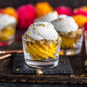 badam halwa served in glass jars topped with whipped cream and garlands of flowers placed in the background