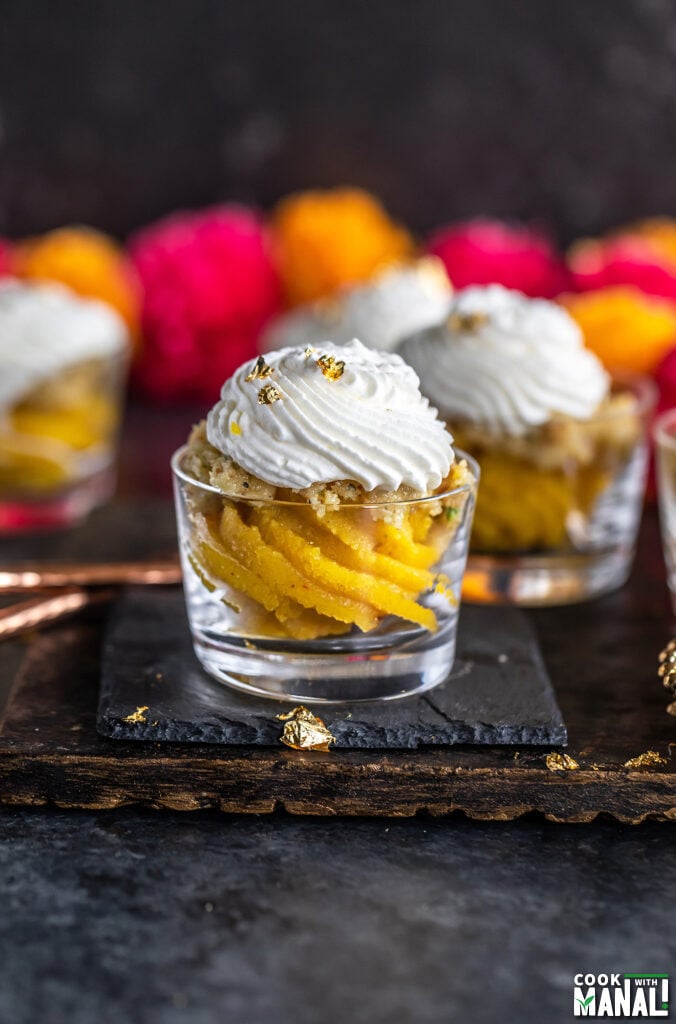 badam halwa served in glass jars topped with whipped cream and garlands of flowers placed in the background