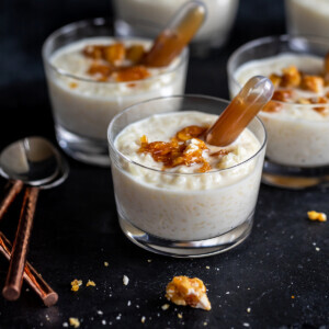 butterscotch kheer served in small jars, garnished with praline and pipettes filled with sauce place on side