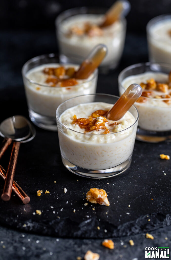 butterscotch kheer served in small jars, garnished with praline and pipettes filled with sauce place on side