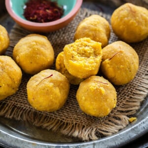 kesar badam ladoo placed on a plate with bowl of saffron strands on the side