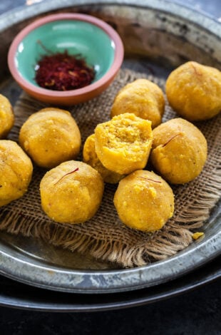 kesar badam ladoo placed on a plate with bowl of saffron strands on the side