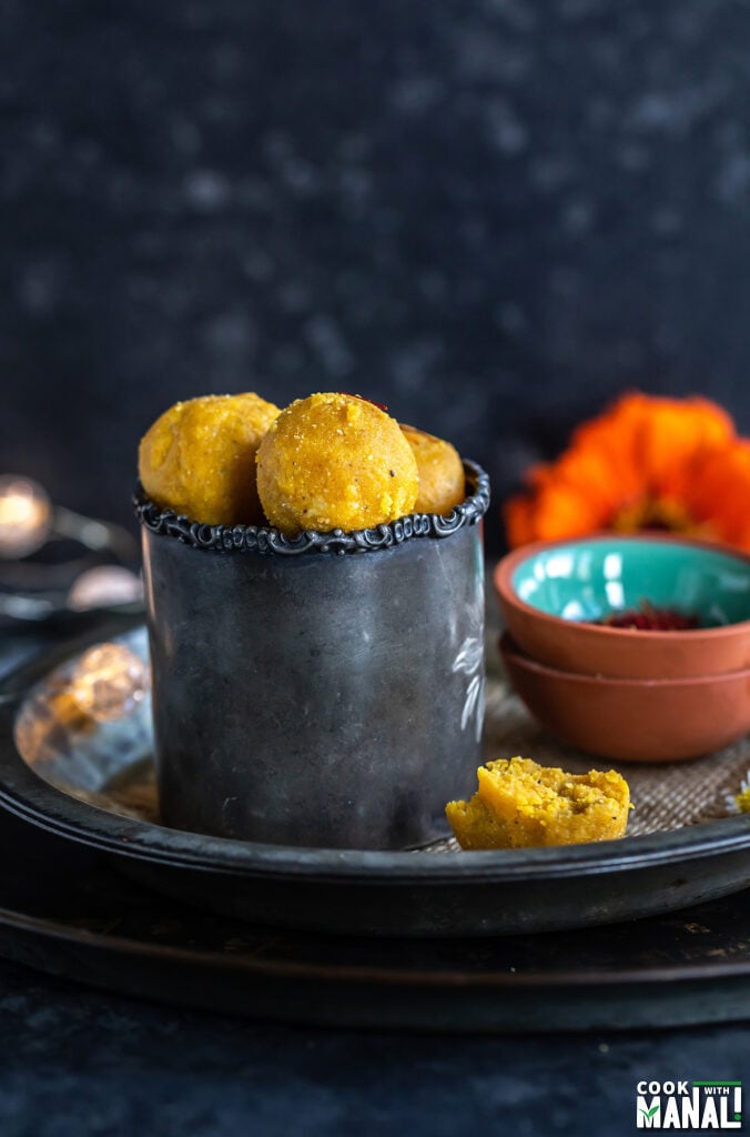 yellow color balls placed in a tumbler with a flower placed on the side along with a bowl of saffron strands