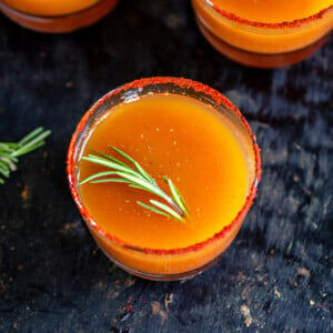 orange color drink garnished with rosemary served in short glasses