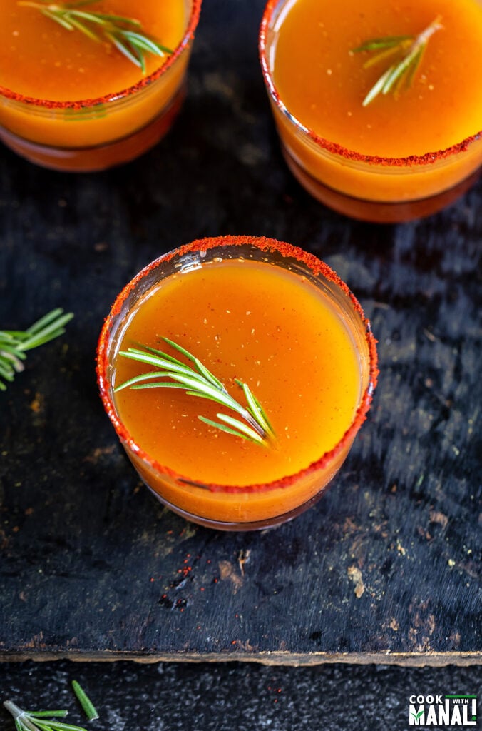 orange color drink garnished with rosemary served in short glasses