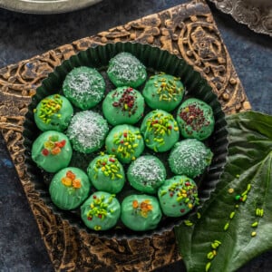 green color balls coated with candied fennel placed in a round plate with paan leaves and some tealights placed on the sides