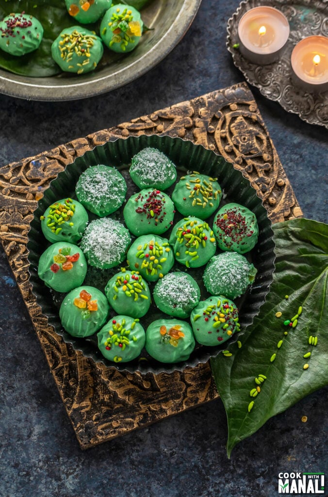 green color balls coated with candied fennel placed in a round plate with paan leaves and some tealights placed on the sides