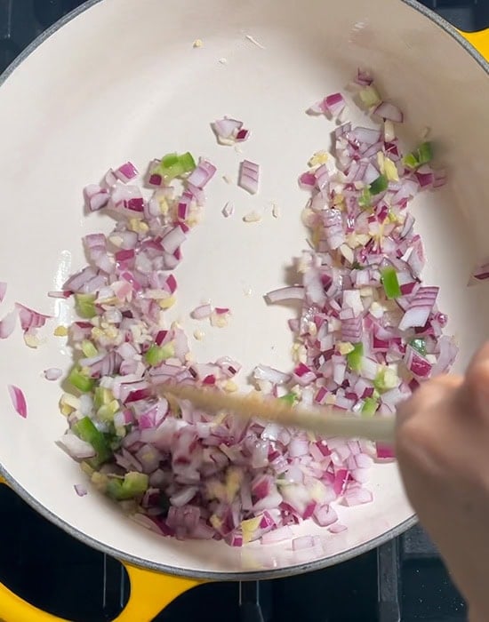 hand stirring onion, garlic, ginger in a pot with a wooden spatula