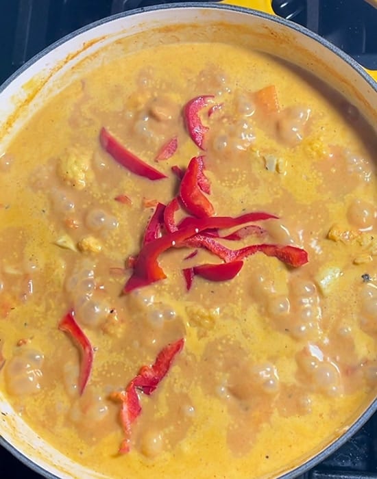sliced red peppers simmering in pot of curry
