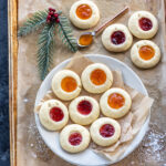 thumbprint cookies arranged on a white plate with more cookies placed in the background