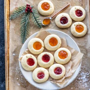 thumbprint cookies arranged on a white plate with more cookies placed in the background