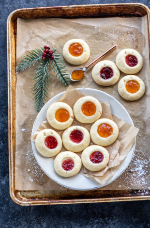 thumbprint cookies arranged on a white plate with more cookies placed in the background